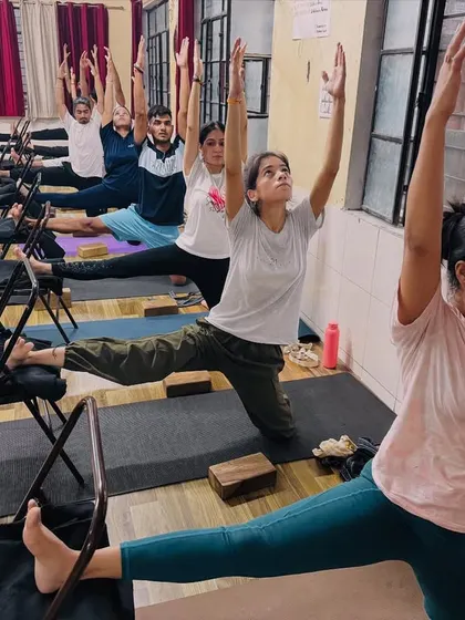 Chairs are versatile props in our classes. Here, students use them to support a modified warrior pose, building leg strength and stability with proper alignment.