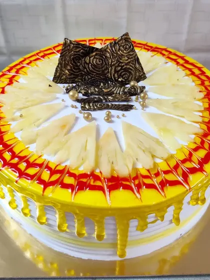 A pineapple cake with a yellow drip glaze. The top is decorated with fresh pineapple slices and chocolate accents.