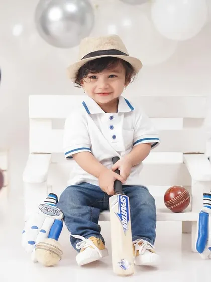 A future cricket star in the making, this little boy is all smiles in a 'Little Cricketer' themed shoot, complete with a bat, balls, and helmet.