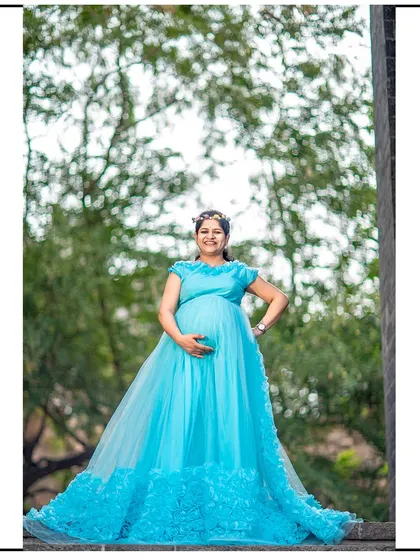 A proud and happy mom-to-be posing in a beautiful light blue gown with a floral-textured train.