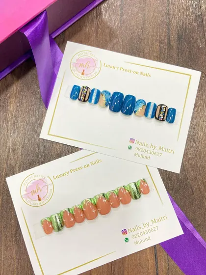 Two different custom press-on sets ready to be shipped. One features a bold blue design with rhinestone accents, while the other has a more earthy green and brown palette.