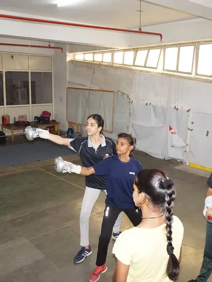 A senior fencer demonstrates the correct form to younger students. We foster a culture where experienced athletes help guide the next generation.