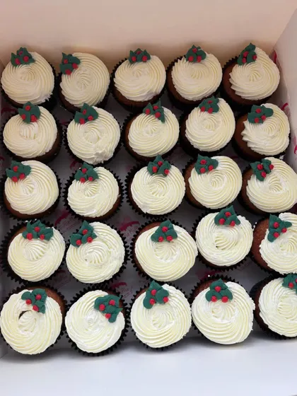 A large batch of simple yet elegant Christmas cupcakes with white frosting and a small fondant holly decoration. Ideal for corporate orders or large family gatherings.