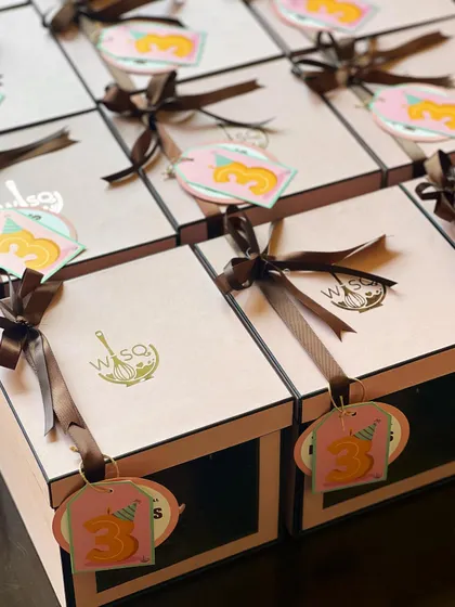 The packaging for our mini cake return favours. Each cake is placed in a pink window box, tied with a brown ribbon and a custom tag celebrating a 3rd birthday.