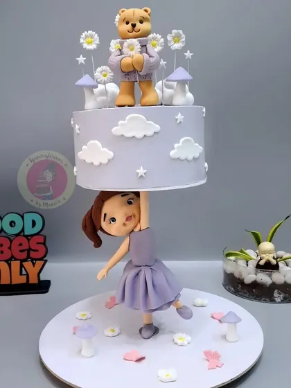 This anti-gravity cake was created for a student's project, featuring a girl holding up a teddy bear-themed tier.