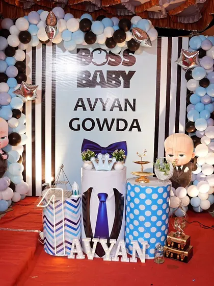 We created this fun Boss Baby setup for Avyan Gowda's first birthday. It features a bold black and white striped backdrop, custom-printed pedestals with tie and suit designs, and a classic blue, white, and black balloon arch.