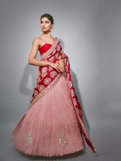 A modern lehenga-saree look. The embroidered red dupatta is draped like a pallu over a simple pink skirt, creating a beautiful contrast and a contemporary silhouette.