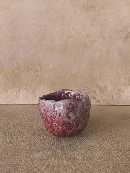 A small, hand-built pinch pot with heart imprints, glazed in a rustic red. This piece is full of love and handmade character.
