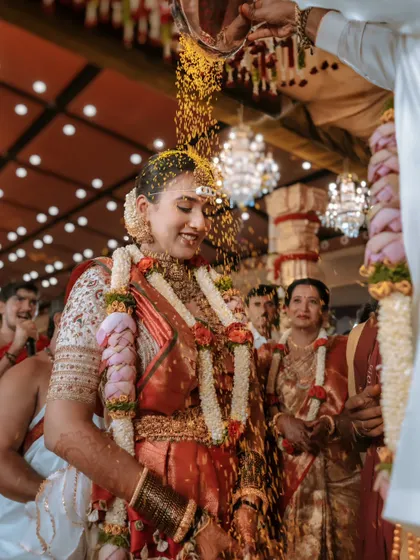 A bride's joyful expression as she is showered with turmeric-coated rice. This candid shot is full of life, color, and the happy blessings of her family.