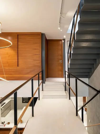 A view from the upper landing in the SOL House shows how the open-riser staircase and bridge create a sense of vertical openness. The material palette combines the raw feel of steel and concrete with the warmth of wood panels.
