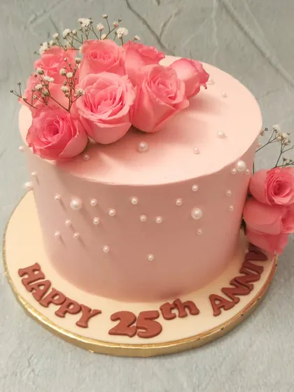 We commemorate a 25th anniversary with timeless elegance. This soft pink cake is adorned with a bouquet of fresh pink roses, sprigs of baby's breath, and scattered pearls, creating a romantic and classic design to celebrate a silver jubilee.