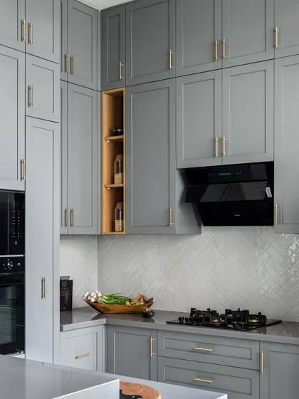 This open kitchen layout follows a shaker style with grey cabinets and white herringbone pattern tiles for the dado. We expanded the kitchen by utilizing deck space, creating a counter with a washing area for the sink and dishwasher.