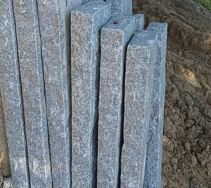 A stack of long, rectangular stone pillars leaning against a pile of earth.