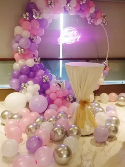 A whimsical birthday decoration with a circular frame and a balloon arch in pastel pink, purple, and silver. This setup is perfect for cake cutting ceremonies and as a photo booth.