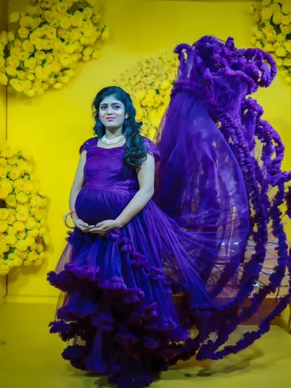 A dynamic shot of a purple maternity gown with a dramatic ruffled trail, flowing in the air against a bright yellow floral backdrop.