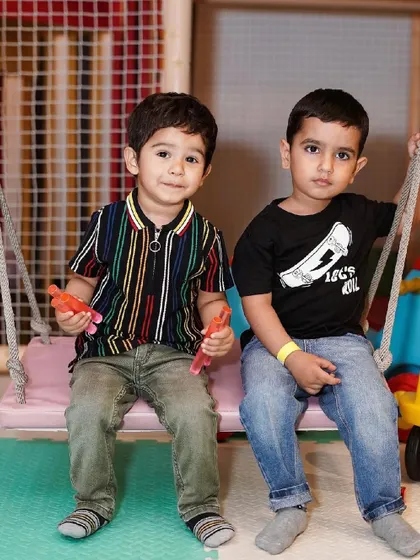 Two young boys sitting on a swing in the play area.