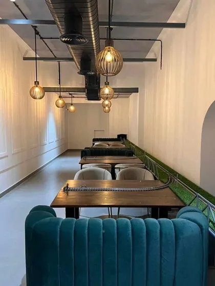 The interior of Kritunga restaurant, featuring unique train-track-themed tables and plush teal channel-tufted booths. The industrial-style pendant lights and exposed ceiling ducts add to the distinctive and memorable dining ambiance.