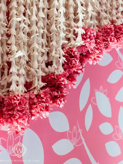 A close-up of the intricate floral work for a half-saree function. The combination of pink carnations and white jasmine against a patterned pink backdrop is simply stunning.