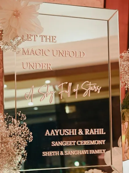 A mirrored welcome sign for a sangeet, with the message "Let the magic unfold under a sky full of stars."