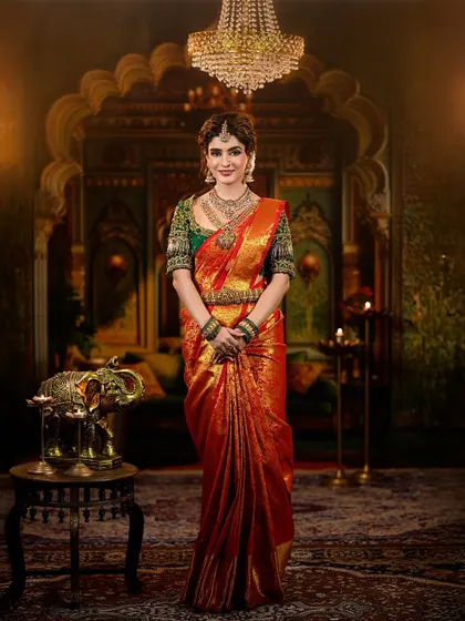 A regal and traditional bridal look featuring a rich red and green Kanjivaram saree. The makeup is defined by warm, shimmery eyes and a deep red lip, perfectly accessorized with temple jewelry.
