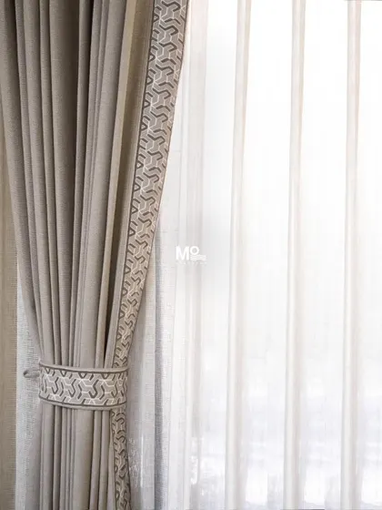 A beautiful example of our custom curtain work, featuring a solid drape with an embroidered geometric border and matching tie-back. This is a testament to our quality products and exceptional service.