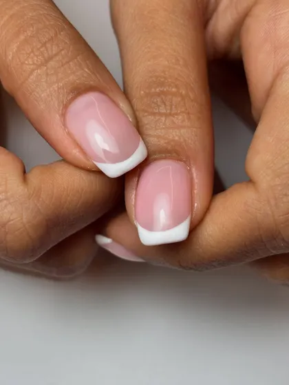 A close-up of a classic French manicure on short, square-shaped nails. This timeless look is all about precision and a clean, healthy-looking finish.