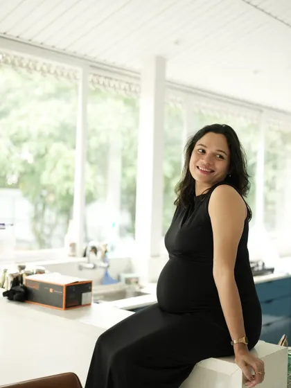 An indoor portrait of the mom-to-be sitting on a kitchen counter, smiling. The natural light from the large windows creates a bright and airy feel.