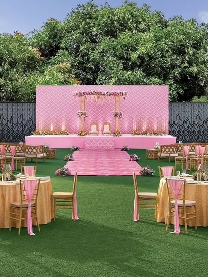 The Vidhi Mandap for the pastel lawn wedding. The stage features a quilted pink backdrop and delicate floral arrangements, creating a soft and romantic focus point for the ceremony.