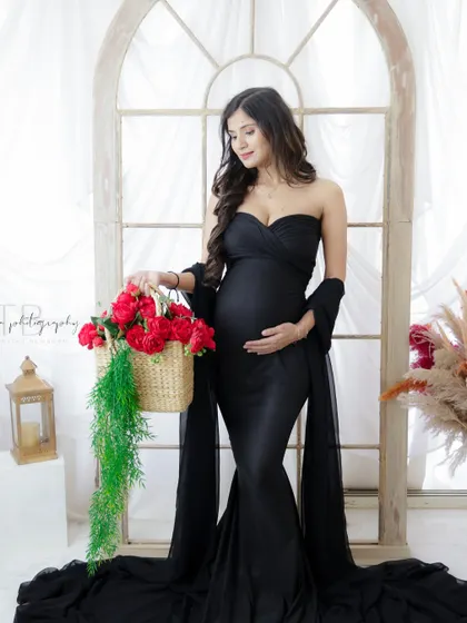 A classic and elegant portrait. The mom-to-be stands by a window, her black gown and a basket of red roses creating a timeless and romantic look.