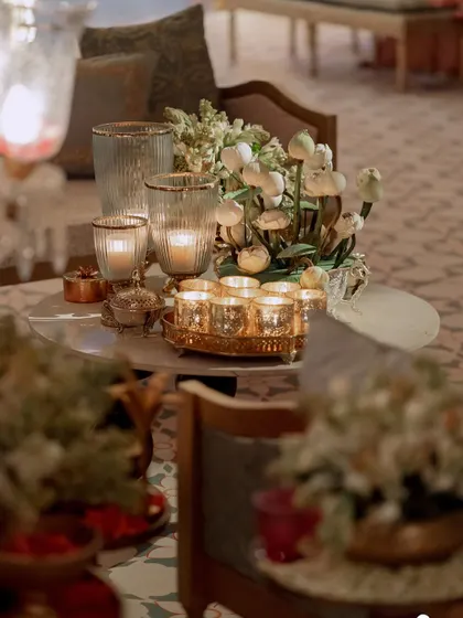 A close-up of a table centerpiece featuring lotus pods and white flowers, surrounded by candles. The warm, ambient lighting creates an intimate and serene atmosphere.