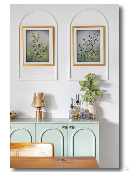 A mint green console with arched cabinet doors sits below two framed botanical prints. This symmetrical and calming composition showcases a love for gentle colors, clean lines, and nature-inspired art.