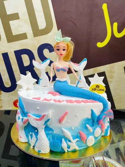 A 2kg mermaid doll cake with a shimmering blue and pink tail, surrounded by fondant shells and stars.