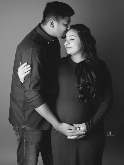 A gentle and loving moment between partners, captured in a simple and elegant black and white portrait. The focus is purely on their connection and the baby they are waiting for.