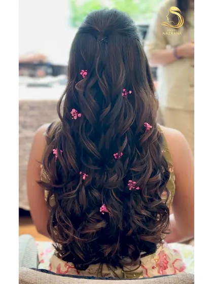 This half-up style combines soft curls with the delicate touch of pink baby's breath, creating a graceful and enchanting Mehendi look.