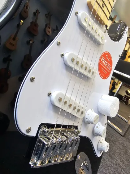 A detailed close-up of the Squier Affinity Stratocaster's pickups and bridge. The three single-coil pickups deliver that signature bright, clear Strat tone.