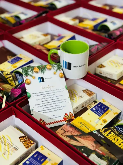 A close-up of a corporate Christmas hamper for Modiwave, featuring a custom-branded mug and a personalized holiday card alongside premium snacks. We ensure every detail aligns with your company's festive message.