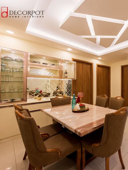 An elegant dining space featuring a marble-top table and a custom crockery unit with rose-gold framed glass shutters and a mirrored backsplash.