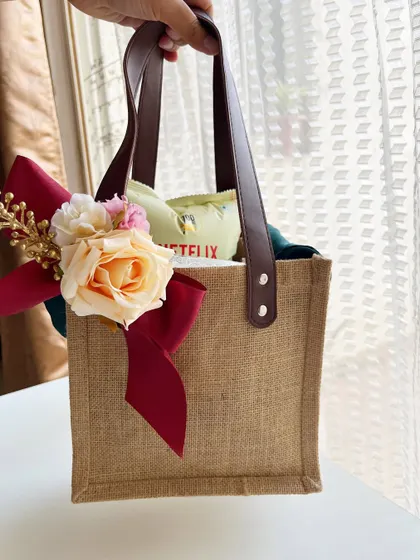 A chic jute tote bag designed as a room hamper for wedding guests. The sturdy leather handles and elegant floral bow make it a stylish and practical gift that guests can use throughout their stay and beyond.