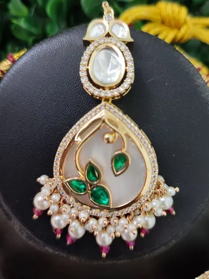 A close-up of a maang tikka with a modern design, featuring a mother-of-pearl inlay with green leaf motifs.