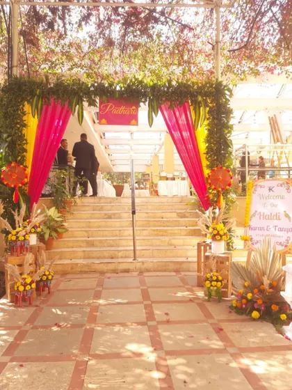 The entrance to a Haldi ceremony, decorated with yellow and pink drapes and lush greenery. The setup creates a warm and inviting welcome for all the guests.