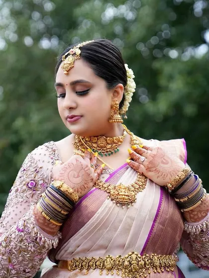 A bride looking serene and beautiful in a classic off-white and purple Kanjivaram saree.