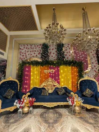 The complete royal Haldi stage setup, including two throne-like chairs and a central sofa. The combination of navy blue, gold, and colorful florals is truly striking.