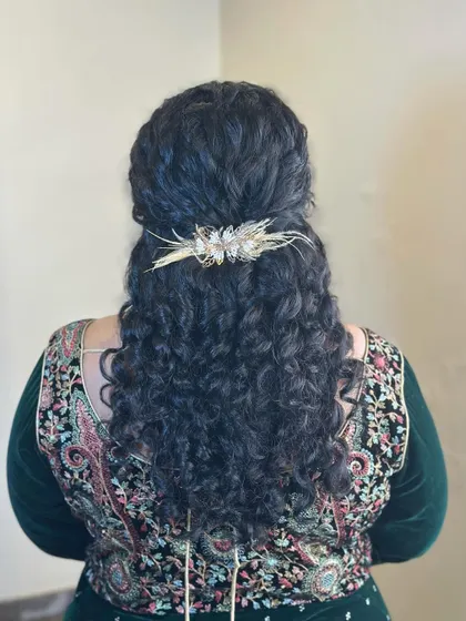 A half-up hairstyle for naturally curly hair, enhanced with a beautiful gold accessory to add a touch of sparkle.
