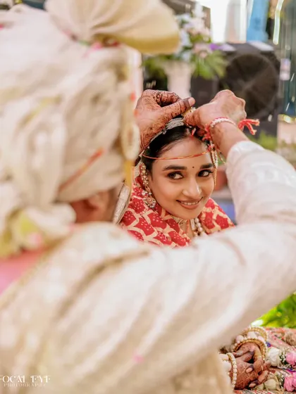 An intimate over-the-shoulder shot of the groom applying sindoor, capturing the bride's beautiful expression.