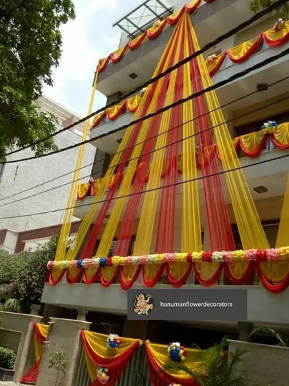 I make sure the festive feeling starts right at the entrance. This is an exterior decoration for a multi-story residence, using bright yellow and red drapes and floral arrangements to make the entire building look ready for a celebration.