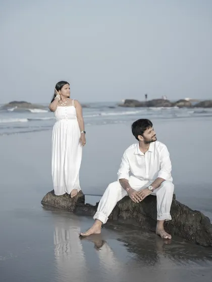 A serene, posed shot of a couple on the rocks at a Goan beach, looking out at the sea.