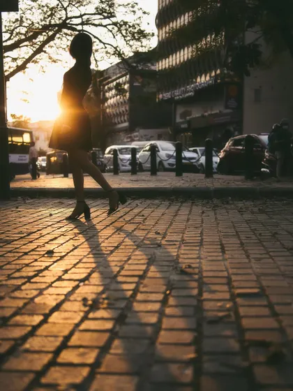 A silhouette of a woman walking on a city sidewalk during the golden hour. The long shadows and warm, setting sun create a beautifully cinematic and atmospheric street photograph.