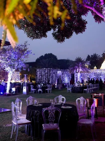 An outdoor view of the enchanted forest party at dusk. The purple lighting on the trees and the shimmering decor elements create a magical contrast against the evening sky.