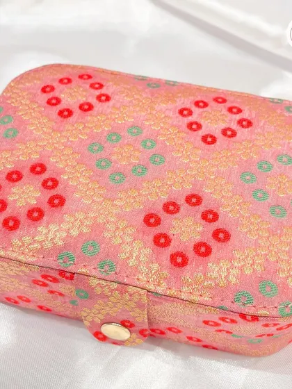 A rectangular jewelry box in a beautiful pink bandhani fabric with a simple button closure.