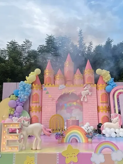 A fairytale unicorn-themed first birthday, complete with a magnificent pink castle backdrop. The setup includes pastel balloon arrangements, fluffy clouds, and adorable unicorn figures, creating a dreamy setting for a magical milestone.